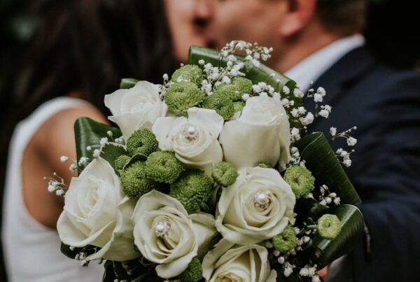 A couple embracing with a focus on a white rose and green floral wedding bouquet.